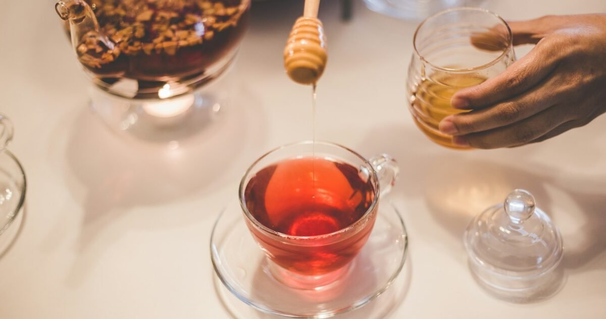 Filet de miel versé avec une cuillère en bois dans une tasse de tisane chaude, contre la toux grasse